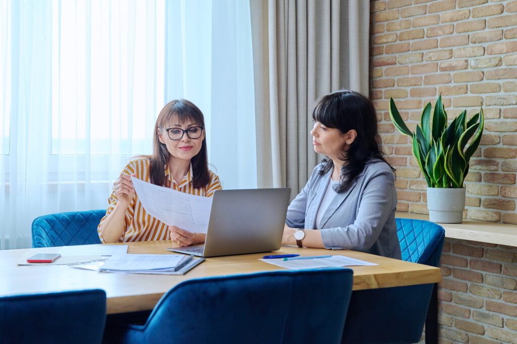 Two mature business women working in office, with papers, laptop